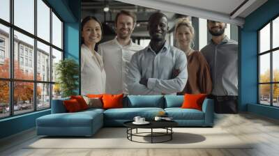 This image shows a team of five diverse professionals posing for a portrait in a modern office setting. They are all smiling and looking at the camera. The team includes two women and three men of var Wall mural