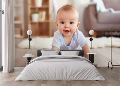 Baby boy crawls on carpeted floor in cozy home environment. Little one is happy, adorable, and cute. Caucasian infant wears clothes, blanket covers his back. Wall mural