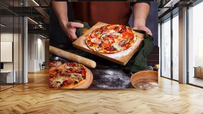 close up hands of chef baker in apron holding a board with hot freshly baked pizza at kitchen. itali Wall mural