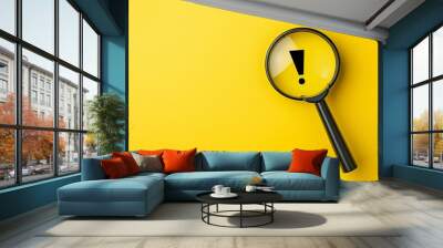 A magnifying glass with a black exclamation mark on a yellow background. Magnifying glass with exclamation mark in warning or threat concept in top view. Wall mural