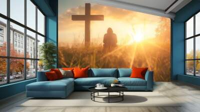 A silhouette of a man kneeling in the middle of a peaceful meadow at sunrise. Man praying at the foot of the cross at sunrise. Wall mural