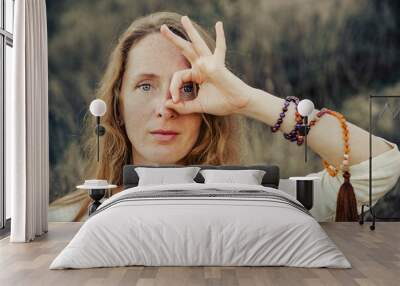 A young woman looks in front of her with a ring made by the fingers of her hand Wall mural