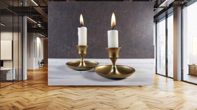 Burning two candles in vintage metal candlesticks on white wooden table against dark stone background.. Wall mural