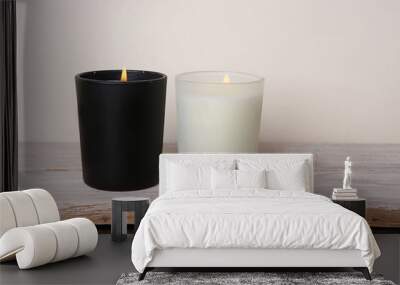 White and black candles. Two burning candles on wooden table against white wall. Wall mural