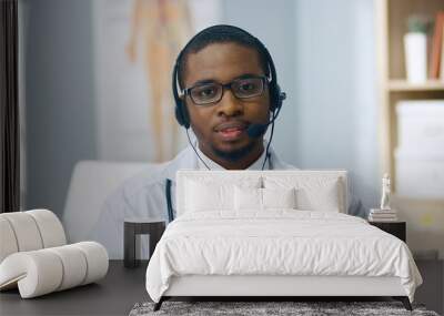 Close up portrait of handsome African American male doctor with stethoscope speaking and explaining in headset with microphone on online consultation sitting in clinic at workplace. Health concept Wall mural