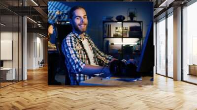 Portrait of professional video editor editing video on his personal computer with two displays in modern video studio. Young man works with headphones Wall mural