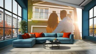 Rear on African American young just-married couple standing at yard of house, hugging and observing second floor. Back view on man and woman in hugs moving in new home. Wall mural