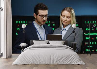 Two fellow programmers stand in server room and discuss work tasks looking at digital tablet. Female system administrator brainstorming with junior IT worker. Wall mural