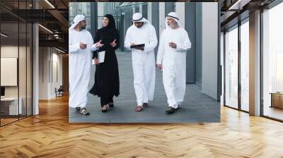 Walking arab people wearing kandura on business location. Arabic businesspeople walking on the city streets wearing dish dasha. Arabian middle eastern smiling while walking and chatting Wall mural