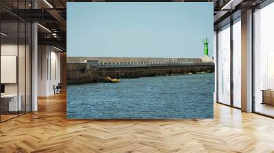 Modern lighthouse pole in green and boat entering sea gates in baltic sea, Pavilosta. Wall mural