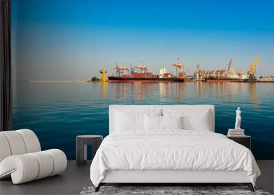 Container ship in the port on the horizon. Port crane loads a container on a ship. Cargo transportation by sea. Wall mural