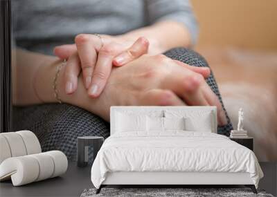 Young woman having rheumatoid arthritis takes a rest sittinng on the couch. Hands and legs are deformed. She feels pain. Selected focus. Wall mural