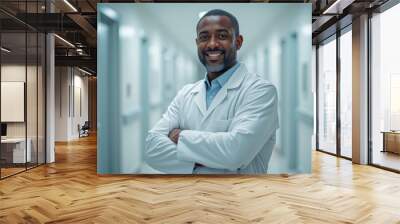 smiling male doctor in white professional clothes standing looking at camera with arms folded on chest, blurred white hospital corridor on background Wall mural