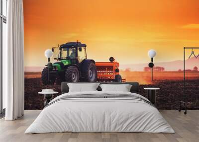 Beautiful sunset, farmer in tractor preparing land with seedbed cultivator Wall mural