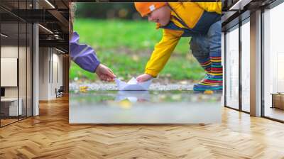 Happy kids girl and boy and colorful rubber boots playing with paper boat in puddle in autumn on nature Wall mural