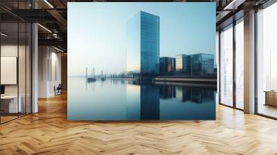 A high-rise building with a contemporary design stands by a riverside, its glass facade reflecting the calm waters and nearby structures, under a clear blue sky Wall mural