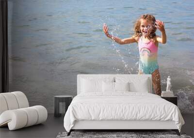 Beautiful happy little girl playing in the waves and splashes on the sea Wall mural