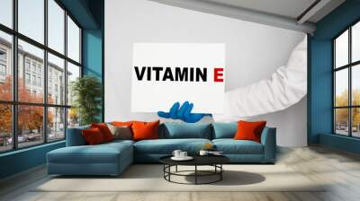 The doctor's blue - gloved hands show the word VITAMIN E - . a gloved hand on a white background. Medical concept. the medicine Wall mural