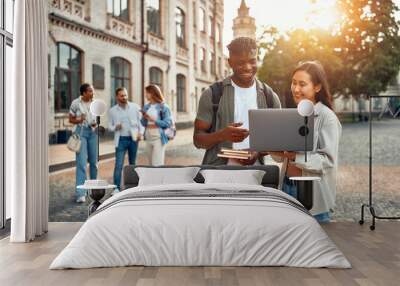 A group of college students collaborating outdoors on campus with a laptop during sunset Wall mural