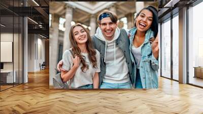 A group of students on the street near the university campus. Three friends are happy to meet, hug and laugh. Wall mural