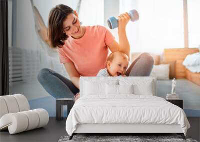 A sports mother is engaged with the child in fitness and yoga at home. The concept of sports, motherhood and an active lifestyle. Young woman in sports training with her child. Wall mural