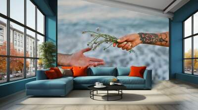 Close-up image of male and female hands with flowers on the background of the sea. Wall mural