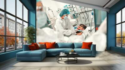 Doctors in protective suits put on a ventilation mask on a sick man with coronavirus disease covid-19, who is in an intensive care unit in a modern hospital. Wall mural