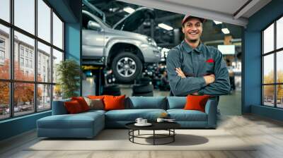 Handsome auto service mechanic in uniform is standing on the background of car with open hood, smiling and looking at camera. Car repair and maintenance. Wall mural