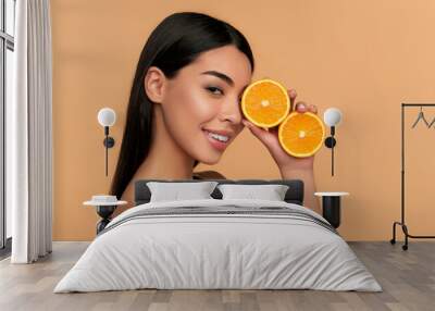 Portrait of Asian girl with shining clean skin of face holding orange halves in white underwear isolated on beige background. Vitamin C cosmetics concept Wall mural