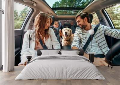 The whole family is driving for the weekend. Mom and Dad with their daughter and a Labrador dog are sitting in the car. Leisure, travel, tourism. Wall mural