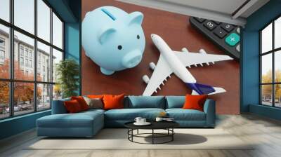 Save money for airplane tickets, planning travel budget concept. Airplane model, piggy bank and calculator on wooden table. Wall mural