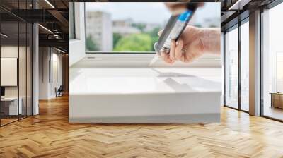 A worker with a construction syringe fills seam between sill and window with silicone sealant Wall mural