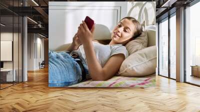 Beautiful young teenage female resting lying on couch using smartphone Wall mural