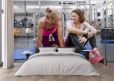 Fitness instructor and mature woman at gym. Female sports instructor and middle-aged woman talking smiling and laughing in health club Wall mural