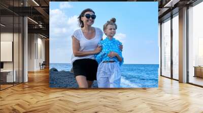 Happy mom and daughter kid hugging walking together along the beach Wall mural