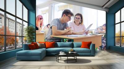 Lesson in class of high school students, female teacher sitting at desk with student Wall mural