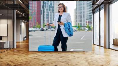 Middle age business woman with suitcase, urban background. Wall mural