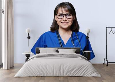 Middle aged female nurse in blue uniform with stethoscope smiling looking at camera Wall mural