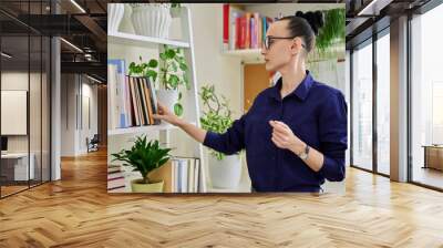 Middle aged woman at home near bookcase choosing book to read learning teaching Wall mural