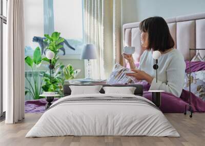 Middle aged woman with cup of coffee in bed Wall mural