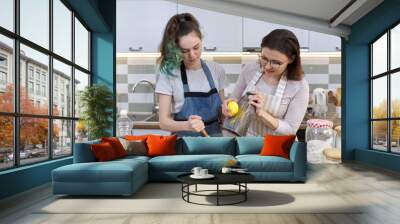 Mother and teenager daughter cook together at home in kitchen Wall mural