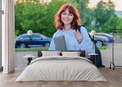 Outdoor portrait of young female college student with backpack, laptop Wall mural