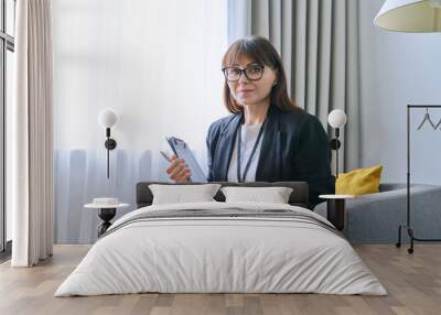 Portrait of middle-aged woman with clipboard sitting in an office chair Wall mural