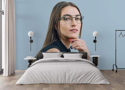 Portrait of young attractive woman with glasses close-up, on blue background, copy space Wall mural