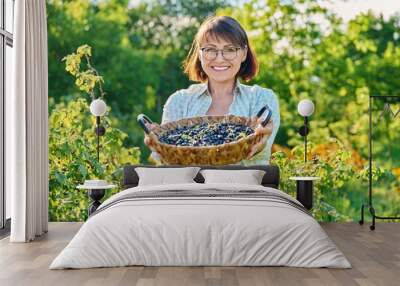 Smiling middle aged woman holding basket of ripe blackcurrants Wall mural