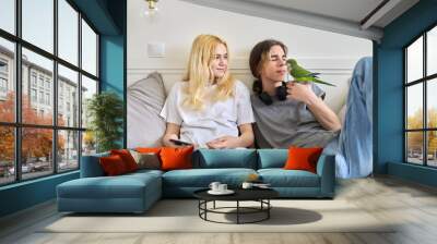 Teenagers sitting at home on the couch playing with a parrot. Wall mural