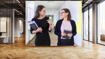 Two colleagues of businesswoman walking and talking on corridor Wall mural