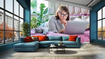 Woman together with cat lying on bed at home, female using laptop Wall mural