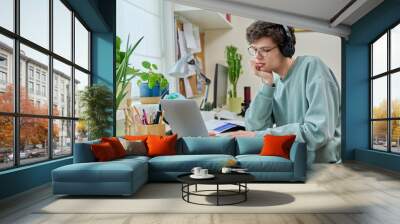 Young male college student sitting at desk at home using laptop Wall mural