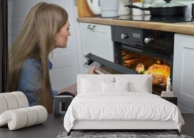 Young woman putting marinated chicken in baking bag in oven Wall mural